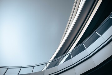 Obraz premium Curved glass railing and sleek metallic exterior of a modern building, set against a light blue sky.