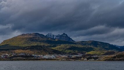 The picturesque Andean Martial mountain range. A snow-covered peak against a cloudy sky. At the foot, on the ocean shore, the city buildings of Ushuaia are visible. Argentina. Tierra del Fuego  