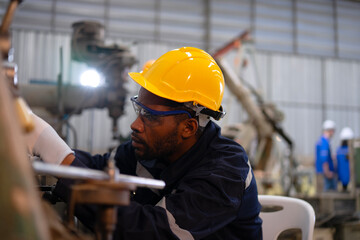 Blue collar workers at machine shop with welding robot arm.