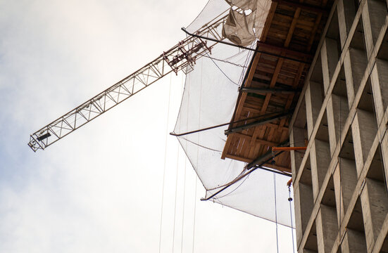 underside view of a construction building, showcasing safety nets overhead to prevent falling objects, with a crane silhouetted against the sky, symbolizing progress and safety in urban development