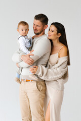 Mother and father hold a one-year-old son of a child in their arms. Portrait of a happy family with a baby in cozy casual clothes for home