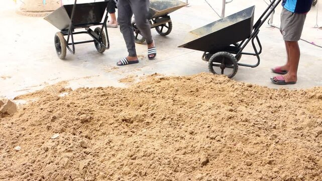 Workers dump sand from wheelbarrows onto the pile