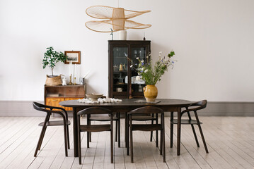 Wooden dining table with black chairs around it is set in a room with a white wall