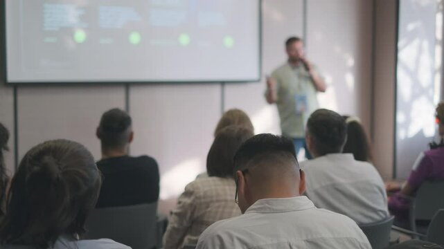 Speaker engages an audience during a presentation in a conference room. The focus is on learning and interaction at a professional event.