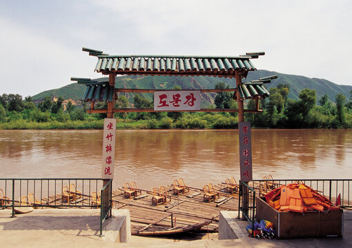 Tumen, Jilin Province, China - August 15, 2009: Summer view of rafts moored on clay water of Tuman River with tile roof entrance door against North Korea Territory
