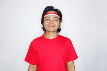 Portrait of an Indonesian man with long hair with a headband and red shirt celebrating Indonesian Independence Day with high nationalism on an isolated white background