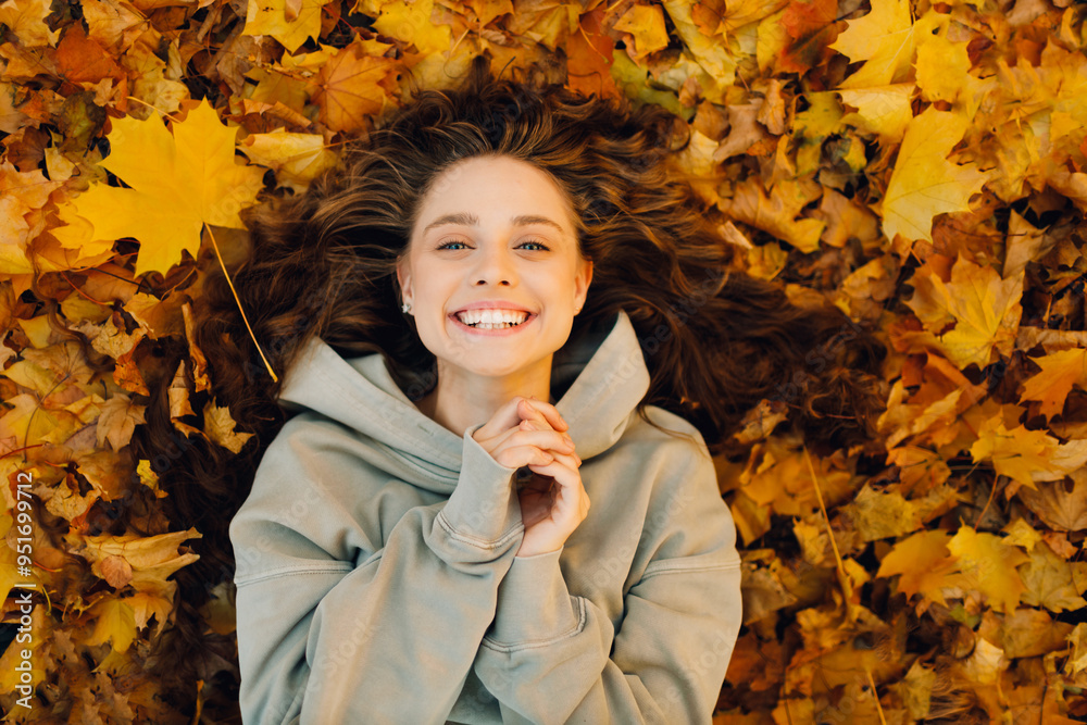 Wall mural smiling young woman lies on the autumn foliage in the forest with the yellow leaves