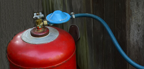 Close-up, a red gas cylinder with a blue regulator and hose connection.Gas supply to the house