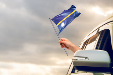 Waving the Nauru flag against the sunrise or sunset from a car driving along a country road. Holding the Nauru flag, traveling by car, on a weekend trip.