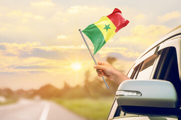 Waving the Senegal flag against the sunrise or sunset from a car driving along a country road. Holding the Senegal flag, traveling by car, on a weekend trip.