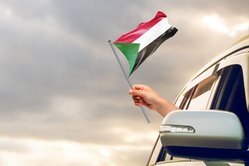 Waving the Sudan flag against the sunrise or sunset from a car driving along a country road....