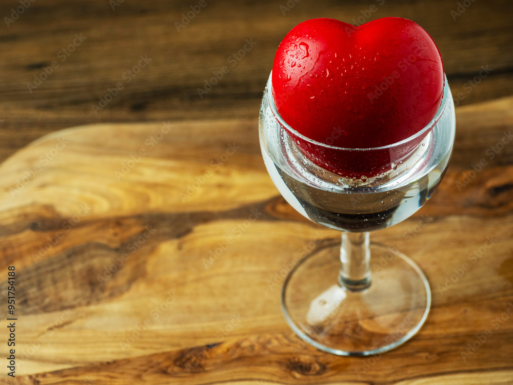 Wall mural a heart is floating in a glass of water. concept of love and romance. glass is on a wooden surface.