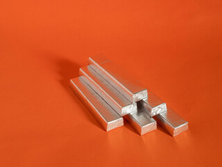 A stack of silver metal bars on a red background. The bars are stacked in a pyramid shape. Invest...