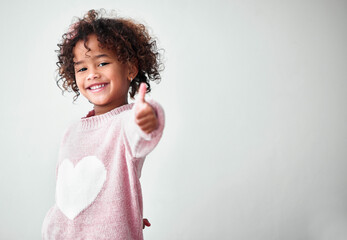 Thumbs up, child or portrait on studio space for yes, approval or happy for agreement. Girl, hand gesture or smile on white background for choice, thank you or appreciation with positivity in Brazil