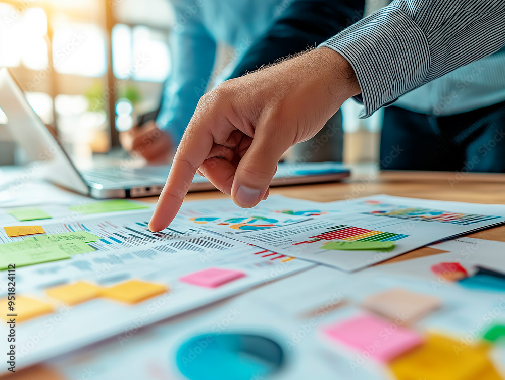 Poster close-up of a person's hand pointing at colorful charts and graphs on a desk.