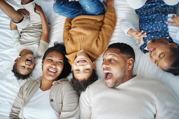 Parents, children and above bed with laughing, love and funny memory for connection in morning at family house. Father, mother and kids with lying, excited and happy for comic joke at apartment