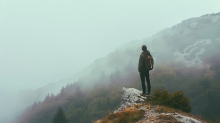 A lone hiker stands on a rocky outcrop, gazing at the misty mountain landscape, surrounded by ethereal fog and dense forest, capturing a moment of introspection and adventure.