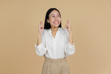 Smiling Woman Crossing Fingers in Hopeful Gesture, Beige Background