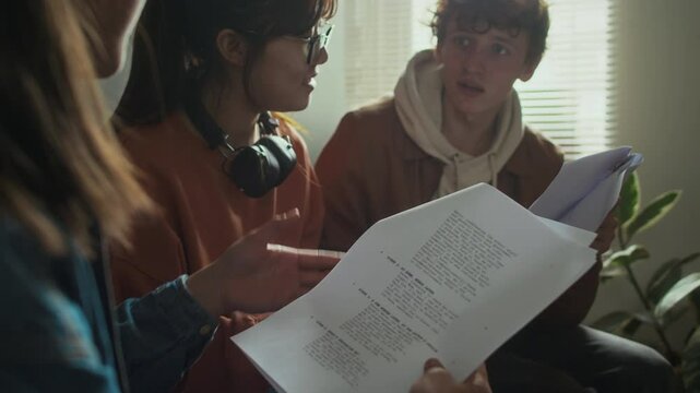Side shot of three diverse cinematography college students discussing filmmaking process and proofreading movie script in dormitory