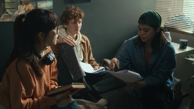 Full shot of group of three diverse cinematography college students gathering in dormitory room to discuss final project and proofread movie script