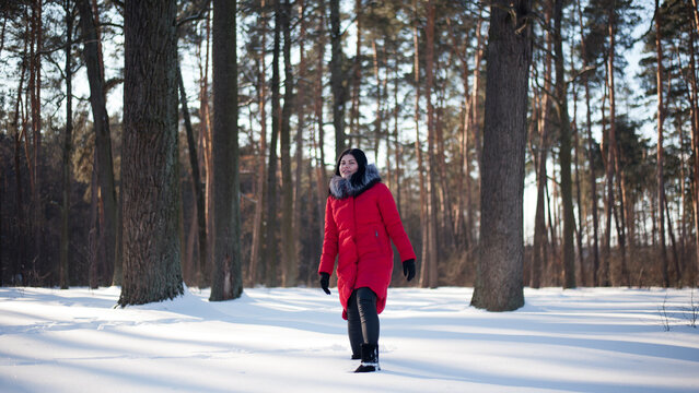 photo with a young woman in the winter forest. girl in a snowy park. in a red jacket on the banks of a frozen river. winter walk in nature. Cold season. Beautiful girl, sunny day. - Powered by Adobe