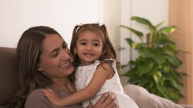 Smiling young mother and daughter hugging at home