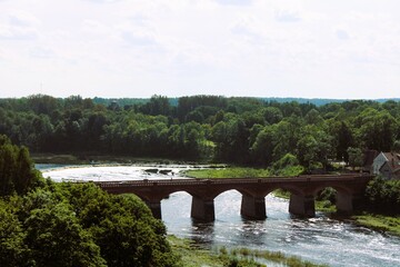 Fototapeta premium top view of an old red brick bridge over a river with a forest in the background