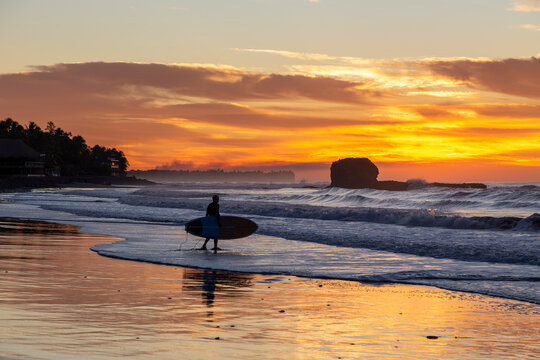 Lone surfer at Playa El Tunco, El Salvador, standing silhouetted against a vibrant sunrise at this popular surf beach destination. The distinctive and iconic rock formation can be seen in the distance