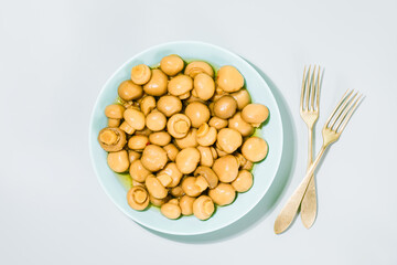 Pickled champignons. Salted, fermented mushrooms on light blue plate, accompanied by vintage forks, highlighting traditional delicacy. Concept of fermented foods, rich in probiotics and rustic flavors