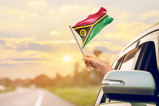 Waving the Vanuatu flag against the sunrise or sunset from a car driving along a country road. Holding the Vanuatu flag, traveling by car, on a weekend trip.