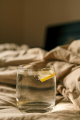 A glass of lemon water resting on a soft, beige bed sheet, evoking a serene and relaxed morning atmosphere