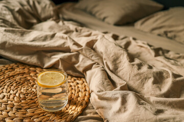 A glass of lemon water resting on a soft, beige bed sheet, evoking a serene and relaxed morning atmosphere