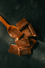 Close-up view of broken chocolate pieces with layers of white and dark chocolate, placed on a wooden spoon against a dark textured background