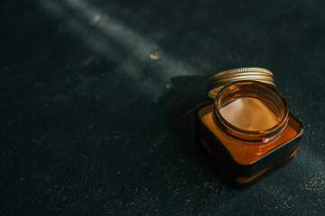 Minimalistic composition of an amber glass candle jar with a metal lid placed on a dark textured surface