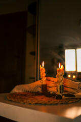 Close-up of two lit candles with melted wax, creating a cozy ambiance against a blurred background of a softly lit room at sunset, capturing the warmth and tranquility of a quiet evening