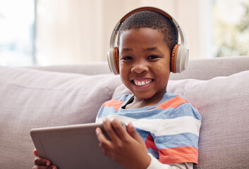Portrait, tablet and happy African kid with headphones for learning, education or listening to music. Face, boy and child with technology for streaming radio, relax and playing game on sofa in home