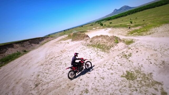 Aerial view from FPV drone. Next shot of a professional motocross rider riding his FMX motorcycle on extreme off-road terrain