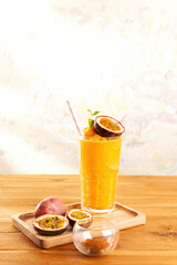 A glass of passion fruit smoothie on wooden tray with fresh passion fruit on abstract colorful wall...