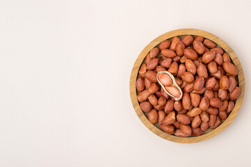 Wooden bowl with whole peanuts with a magnifying glass.  Top view, on a light background, horizontal, free space for text.