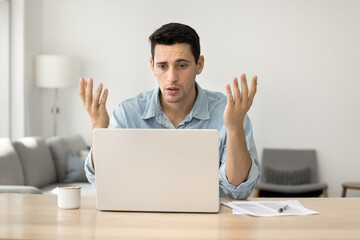 Concerned puzzled Latin freelance worker man looking at laptop with confused hand gesture....