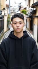 Obraz premium A young Asian man poses in a black hoodie within a vibrant urban alleyway