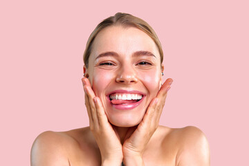 Portrait of a cheerful beautiful young woman with healthy glowing skin and snow-white teeth playfully posing for the camera on a soft pink background.