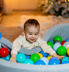 Toddler playing happily in colorful ball pit at home during winter. A joyful toddler is surrounded by colorful balls while playing in a cozy indoor ball