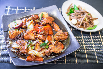 Andong Jjimdak on Square Plate with Sliced Red Chili Pepper, and Blurred Jangjorim in the Background with Table Setting
