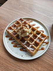 delicious waffle with vanilla ice cream and caramel sauce on it sits on a plate.