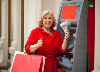 An elderly woman with shopping blonde is on the background in shopping center ATM
