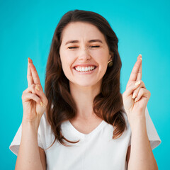 Fingers crossed, good luck and hope with woman on blue background for superstition or wish. emoji, eyes closed and giveaway with happy person isolated in studio in anticipation of competition win