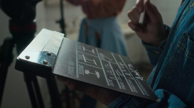 Side closeup of hands of faceless stage manager holding film slate and filling it out with chalk while preparing to shoot movie in set indoors