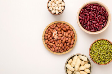 Assortment of legumes in bowls on a light background, top view. Horizontal, free space for text. Mung beans, chickpeas, peanuts, beans, lentils.