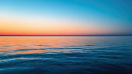 Fototapeta premium A calm sea at dusk, with the sky transitioning from blue to deep orange and the water reflecting the colors.